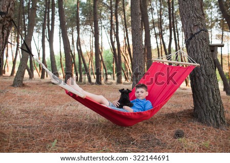 Boy relaxing with family dog in a hammock in pine forest