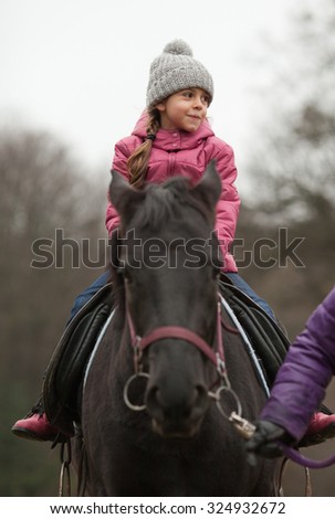 Little girl riding on a horse. Adult leading horse by bridle
