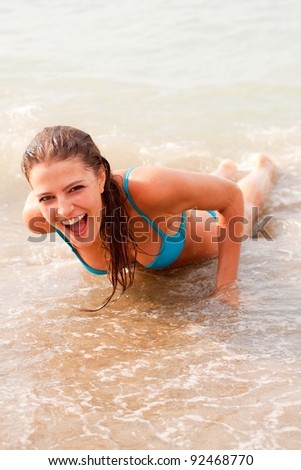 The beautiful young girl in a bathing suit smiles lies on sand at the sea