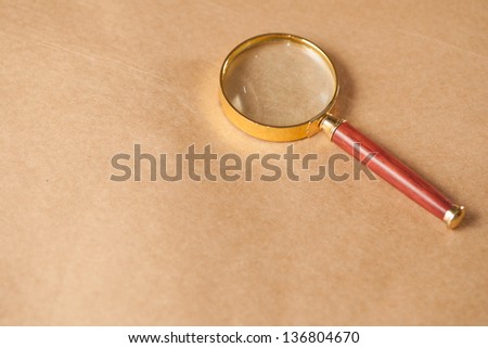 A golden and red magnifying glass on a brown paper background.