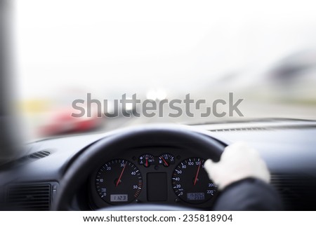 Driving a car in high speed, first person view. Hand on steering wheel of a car driving on a road. Focus on clocks.