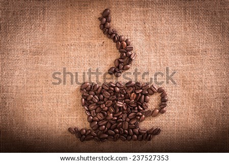 Cup of coffee stacked with coffee beans against burlap canvas.