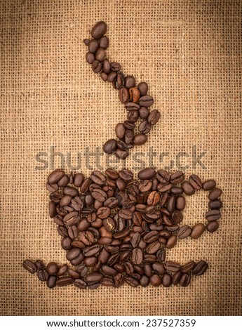 Cup of coffee stacked with coffee beans against burlap canvas.
