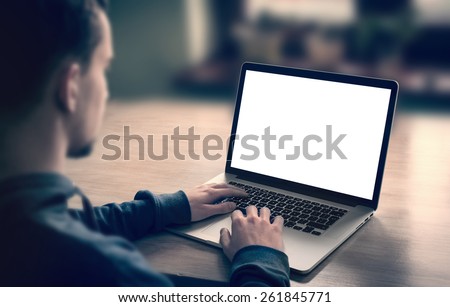 Man using, working on laptop with blank screen in home living room.