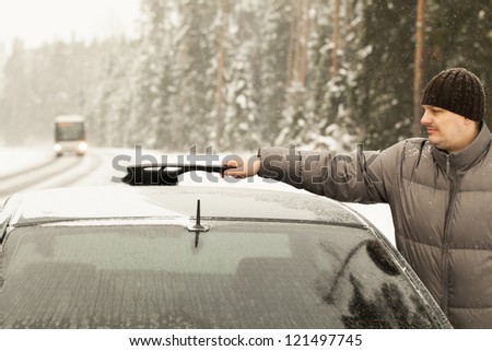 Man cleans the car out of the snow in snow storm