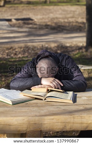 Man lying asleep on books outside on a bench