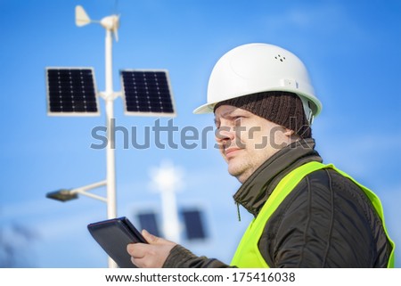 Electrical Engineer with tablet PC near street lighting with solar panels and wind generator