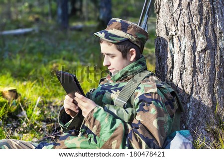 Army recruit with tablet PC in forest near tree.