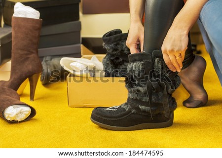 Women fit on boots near heap of shoes boxes