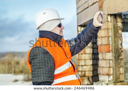 Engineer with tablet PC take a picture near unfinished building