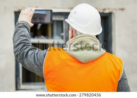 Construction inspector with tablet PC near building with broken window
