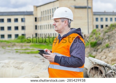 Construction Engineer with tablet PC near building