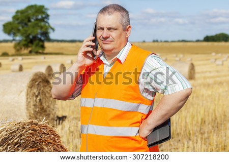 Farmer talking on smartphone near hay bales