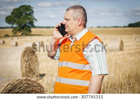 Farmer talking on smartphone near hay bales