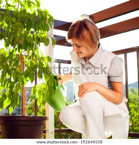Beautiful young woman is taking care about plants, on the balcony.