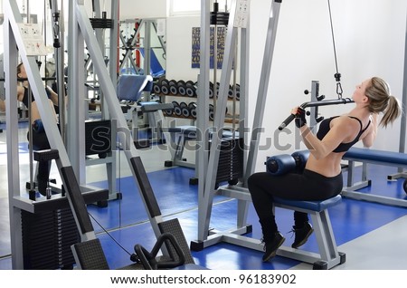 Beautiful and young woman in motion working out in the gym on lat machine.