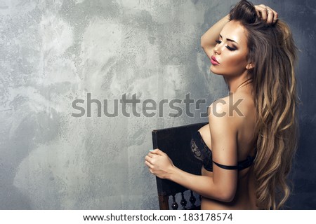 Beautiful sexy blonde woman standing, wearing black sensual lingerie, looking away.