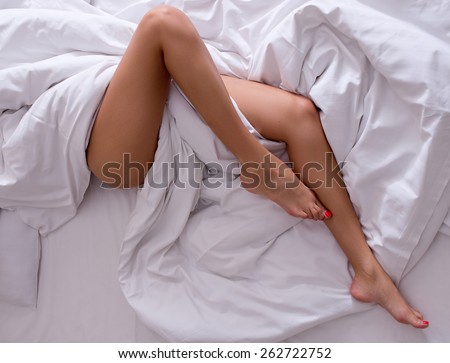 Woman legs on the bed in white bedclothes