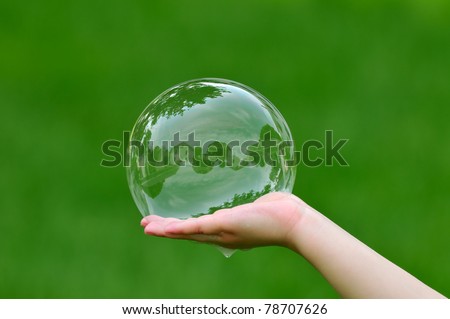 Child holding soap bubble with house reflection
