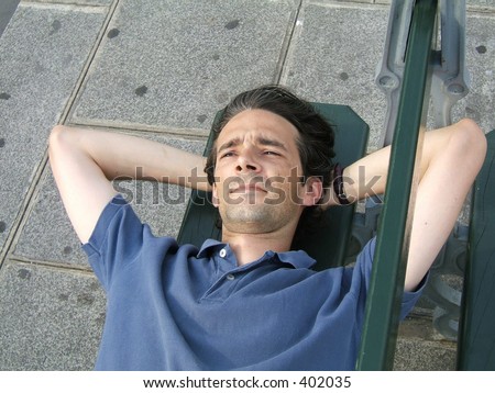 A man laying on a street bench is thinking and smiling