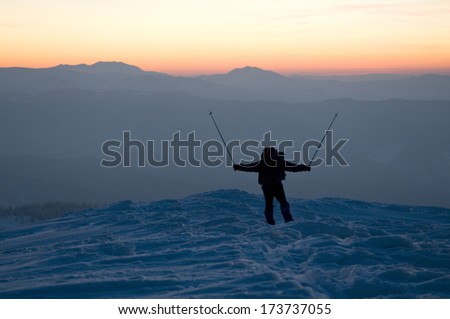 Happy man (tourist) is situated on the top of mountain covered with snow. Sunset and outlines of the mountains are in the background.