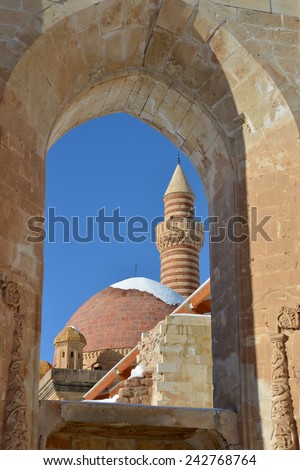 This is a view of Ishak Pasha Palace through the window of surrounded wall. The minaret and domes are sitiuated against the blue sky background.