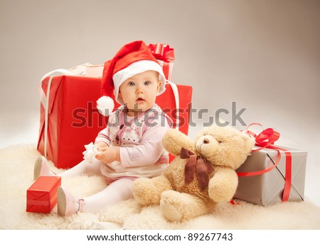 Surprised baby siting with gift boxes and a teddy bear