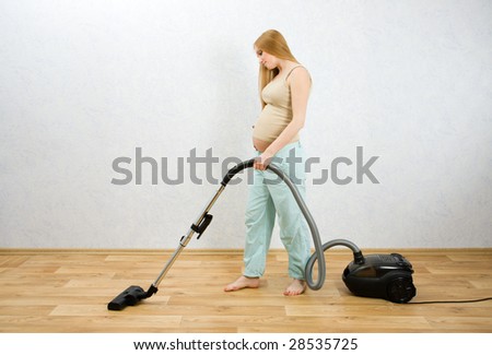 Pregnant caucasian woman cleaning floor with vacuum cleaner