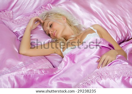Young caucasian woman sleep in bed on pink silk sheets