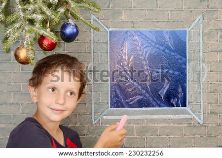 Christmas decoration and smiling boy draws on the window frost work