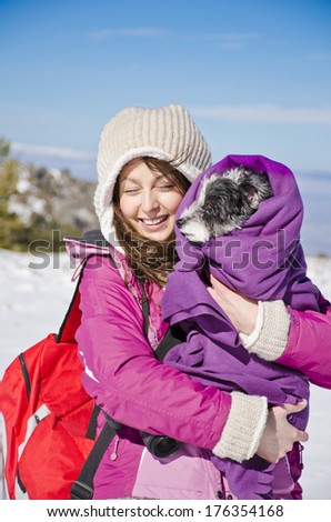 Portrait on beautiful girl in the winter forest hugging her little dog wrapped in a blanket