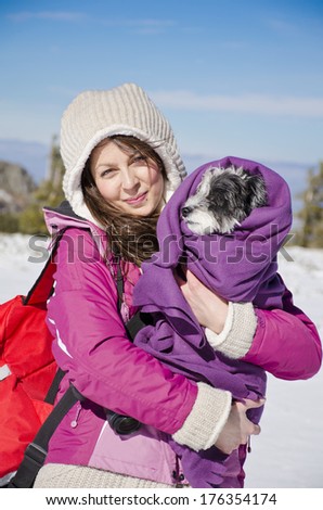 Portrait on beautiful girl in the winter forest hugging her little dog wrapped in a blanket