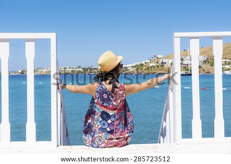 Portrait of  young woman with straw hat sitting on a wooden stairs and watching the sea