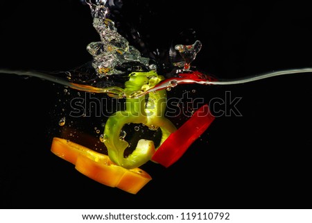 Slices of fresh red, green and yellow pepper falling into the water with a splash on black background