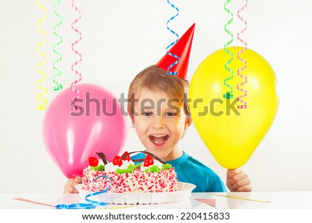 Little smiling boy in holiday cap with a birthday cake and balloons