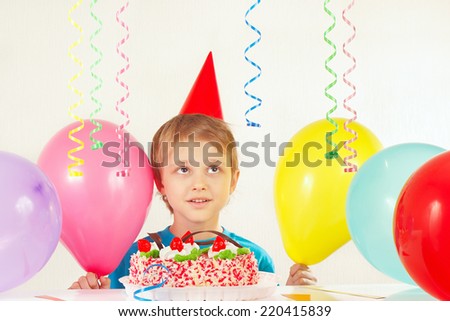 Little boy in holiday hat with a festive cake and balloons