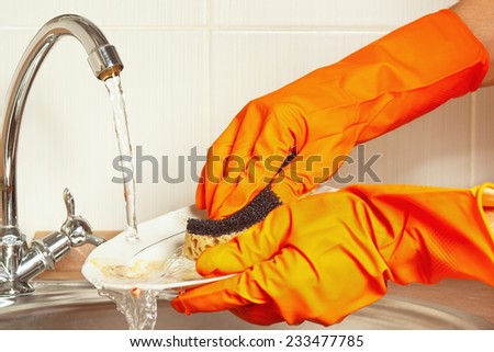 Hands in gloves wash the dishes under running water in the kitchen