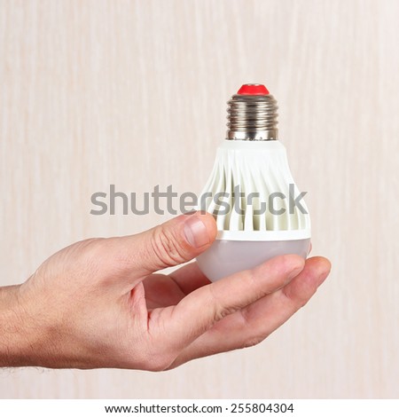 Hand holding a light bulb on a light wood background