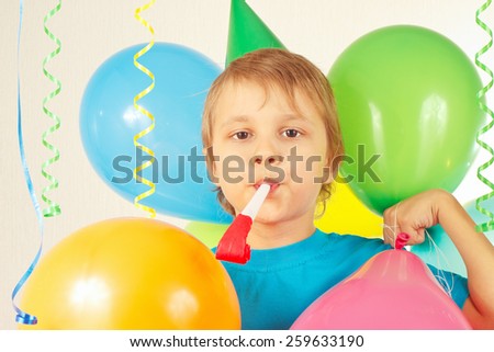 Little cute boy in holiday hat with whistle and festive balloons and a streamer