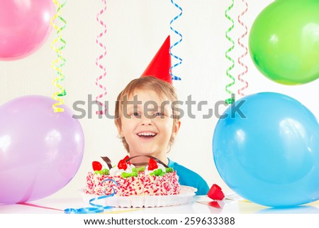 Young boy in festive hat with a birthday cake and balloons