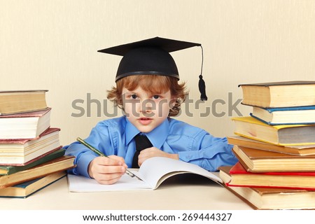 Little boy in academic hat writing pen in a notebook among the old books