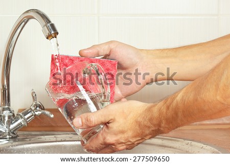 Hands with sponge wash the glass over the sink in the kitchen