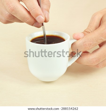 Hands mixing with a spoon of black coffee in the cup