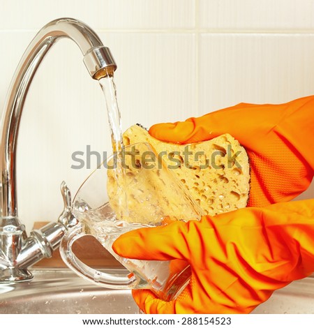Hands in gloves wash the dirty glass under running water in the kitchen
