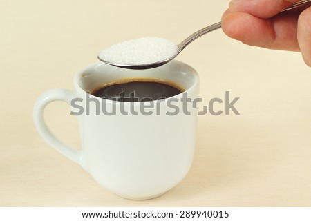 Hand pours sugar from a spoon in a coffee cup