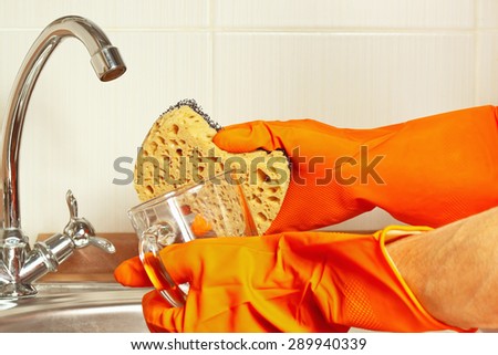 Hands in rubber gloves with sponge and dirty cup over the sink in the kitchen