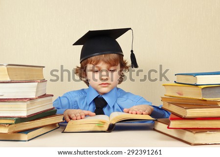 Little serious boy in academic hat reading an old books