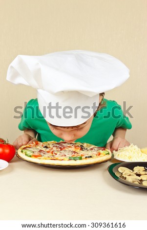 Little funny chef sniffing the aroma of cooked pizza
