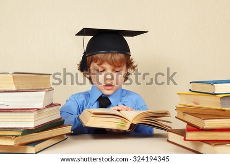 Little smart boy in academic hat turns the pages of an old book