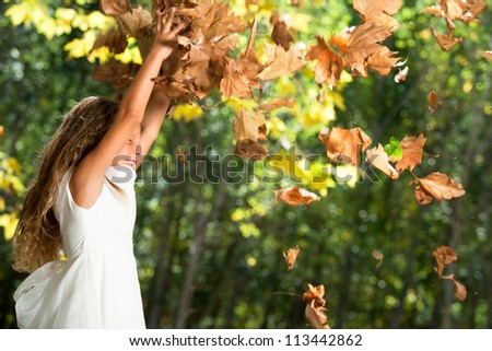 Young happy girl playing with autumn leaves in park.